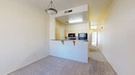This one-bedroom, one-bathroom unit is thoughtfully arranged across a single floor, offering a functional and efficient layout. The entryway features wood-look vinyl flooring that transitions seamlessly into the carpeted living area, creating a welcoming introduction to the space. A pendant light fixture hangs above the open living area, which flows directly into the kitchen via a raised peninsula counter with granite-style countertops — ideal for casual dining or food preparation. The kitchen is equipped with light wood cabinetry, a built-in microwave, and a refrigerator, all illuminated by overhead lighting. A hallway connects the main living space to the private bedroom and bathroom. The generously sized primary bedroom is carpeted and filled with natural light from a large window dressed with vertical blinds, and includes access to a closet. The full bathroom features wood-look tile flooring, a light wood vanity with stone-style countertops, and grab bars for added accessibility. Throughout the unit, neutral cream-toned walls and consistent finishes create a clean, cohesive aesthetic that offers a versatile canvas for personalization.