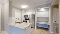 This well-appointed one-bedroom, one-bathroom residence at 1 Stonebridge Cir in Little Rock, AR offers a thoughtfully designed single-floor layout. The open-concept kitchen is a standout feature, showcasing granite countertops, a double-basin sink, white shaker-style cabinetry, a subway tile backsplash, and a full suite of stainless steel appliances including a refrigerator, electric range, and microwave. A built-in desk nook with matching granite countertop and cabinetry adds a functional workspace just off the kitchen. Light hardwood-style flooring runs through the kitchen, while plush carpet extends into the combined dining and living area, which is finished with crown molding and ceiling fans throughout. The living area opens to a private balcony through a sliding glass door, offering pleasant outdoor views. The bedroom is carpeted and well-lit by natural light from multiple windows, and includes access to a walk-in closet. The bathroom features a granite-topped white vanity, wood-look vinyl flooring, and a full tub-shower combo. A dedicated laundry area and utility room round out the functional layout of this efficiently designed home.