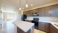 Located at 1570 DeSanctis Pl in River Falls, Wisconsin, this two-story home offers a well-designed layout spread across two floors. The main level features an open-concept living and kitchen area finished with light hardwood flooring that enhances the bright, airy atmosphere. The kitchen is a standout space, outfitted with rich dark-brown shaker-style cabinetry, light countertops, black appliances including a refrigerator, electric range, microwave, and dishwasher, and a generously sized center island with pendant lighting overhead. A wall-mounted mini-split unit provides additional climate control, and a door leads directly outside. The living room is bathed in natural light from large windows that offer views of the surrounding landscape, complemented by wall sconce lighting and baseboard heating. The upper floor hosts both bedrooms, including a spacious primary bedroom with multiple closets, a ceiling fan, and ample room to accommodate a full furniture arrangement. The second bedroom also enjoys natural light and outdoor views through a large window. Two full bathrooms with clean, modern finishes serve the residence. Soft carpeting in the bedrooms contrasts nicely with the hard flooring on the main level, creating a comfortable, cohesive feel throughout.