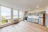 Located at 401 Union Ave SE in Olympia, Washington, this one-bedroom, one-bathroom unit offers a well-designed layout across a single floor. The open-concept living and kitchen area is the heart of the unit, flooded with natural light through large, floor-to-ceiling windows that frame views of the surrounding Olympia cityscape and greenery. Light-toned luxury vinyl plank flooring runs throughout, creating a clean, cohesive aesthetic.

The kitchen is outfitted with sage-green cabinetry, stainless steel appliances including a range, dishwasher, and refrigerator, as well as an overhead ventilation hood and open shelving. A wall-mounted HVAC unit provides climate control adjacent to the living area windows.

A hallway connects the main living space to the private bedroom, which features a compact interior window and additional exterior windows that bring in natural light and outdoor views. The bathroom includes a full tub-shower combination, a single-sink vanity with matching sage-green cabinetry, and clean white finishes throughout. An in-unit laundry area adds everyday convenience. The overall ambiance is modern and bright, with a neutral color palette that maximizes the sense of openness throughout the unit.
