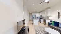 This well-designed 2-bedroom, 2-bathroom single-story unit offers a thoughtful layout that maximizes its footprint with clean, contemporary finishes throughout. The open-concept living and kitchen area serves as the heart of the home, featuring light hardwood flooring, recessed lighting, and a ceiling fan. The kitchen is equipped with stainless steel appliances—including a French door refrigerator, gas range, microwave, and dishwasher—complemented by white shaker cabinetry, a gray subway tile backsplash, granite countertops, and a center island with seating. The living room receives natural light through a large window and opens directly to the front entry. Both bedrooms are bright and comfortable, each with hardwood floors, ceiling fans, and generous windows fitted with blinds. One bedroom features a private exterior door and an adjoining walk-in closet with built-in shelving. The bathrooms are finished with marble-look tile flooring and tub surrounds, white vanities, and clean, modern fixtures. A dedicated in-unit laundry area houses a full-size washer and dryer. Two hallways connect the rooms efficiently, and an additional closet provides extra storage space.