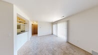 This single-floor unit offers a well-organized layout encompassing a living room, bedroom, kitchen, bathroom, and two closets. The living room is a bright, open space finished with neutral-toned carpet and features a full-width sliding glass door dressed with vertical blinds, allowing generous natural light to filter in and providing outdoor access. The entry area connects seamlessly to the main living space, which is defined by clean white walls and a simple, functional design.

The galley-style kitchen is efficiently arranged with white cabinetry, dark laminate countertops, and hardwood-style flooring. It is equipped with black appliances, including a refrigerator and range, along with ample upper and lower cabinet storage. An electrical panel is accessible within the kitchen corridor.

The bedroom is a comfortable, carpeted room with a window offering natural light and outdoor views, maintaining the unit's consistent neutral color palette. Two closets provide practical storage throughout the unit.

The bathroom features a dark laminate vanity countertop with an integrated sink, a large mirror, and a tiled shower-tub combination with a grab bar. Hardwood-style flooring completes the bathroom's clean, functional aesthetic. Overall, the unit presents a straightforward, efficient living environment.