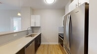 Located at 13 Shetland Ave in Boston's Roxbury neighborhood, this modern single-floor unit offers a thoughtfully designed layout with clean finishes throughout. The kitchen is outfitted with stainless steel appliances, including a French door refrigerator, range, and dishwasher, complemented by two-toned cabinetry — white upper cabinets and dark lower cabinets — set against a neutral tile backsplash and light quartz countertops. A breakfast bar peninsula opens the kitchen toward the living area, which is illuminated by natural light streaming through large windows with views of surrounding greenery. Pendant lighting over the peninsula adds warmth to the space. Hardwood-style flooring flows throughout the main living areas and bedrooms, lending a cohesive, contemporary feel. The bedrooms are well-sized, with one featuring a mirrored sliding closet door and another offering direct access to an adjoining hallway. A conveniently located in-unit stacked washer and dryer adds everyday practicality. The bathrooms are finished with large-format tile flooring, white cabinetry with brushed hardware, and a full tub-shower combination. The overall ambiance is bright, clean, and modern, making this a well-appointed urban residence.