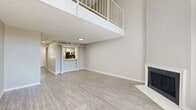 This two-story residence is thoughtfully designed across two balanced floors, offering a functional and modern layout. The main floor centers around a spacious living room with striking double-height ceilings, a white-framed fireplace, and light wood-look flooring that extends throughout. A pass-through kitchen on this level features white shaker cabinetry, quartz countertops, a subway tile backsplash, stainless steel appliances including a refrigerator, range, microwave, and dishwasher, all complemented by a double-basin sink. A hallway connects the main living areas to a full bathroom, finished with a white vanity, quartz countertop, and a tub-shower combo with wood-look flooring. Two closets on the main floor provide ample storage. Ascending the white-railed staircase, the upper floor opens to a generously sized loft-style room with vaulted ceilings and plush carpeting, overlooking the living area below. A second kitchen and an additional bathroom with angled ceilings are also found on this level, adding versatility to the upper floor. Neutral gray tones and textured ceilings throughout create a clean, cohesive aesthetic, while recessed lighting ensures each space is well-illuminated.