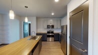 This single-floor unit offers a thoughtfully designed layout that balances functionality and contemporary style throughout. The kitchen serves as a standout feature, combining two-tone cabinetry — dark lower cabinets paired with light upper cabinets — with warm butcher block countertops. A central island with an integrated sink and pendant lighting above provides additional workspace and a natural gathering point. Stainless steel appliances, including a range, over-the-range microwave, and refrigerator, complete the kitchen. Light wood-look flooring runs throughout the main living areas, contributing to a clean, cohesive aesthetic.

The open living area adjoins the kitchen, offering a versatile space with recessed lighting and a sliding door that introduces natural light and outdoor access. The bedroom features plush carpet flooring, a ceiling fan with a light fixture, and a window with blinds that allows natural light to filter in.

Two bathrooms serve the unit. The full bathroom includes a tiled tub-and-shower combination, a toilet, and a vanity with a wood-tone countertop, dark cabinetry, and a mirror. The half bathroom mirrors a similar vanity design and maintains the same light flooring found throughout. Overall, the unit presents a modern, move-in-ready environment with consistent finishes across all spaces.