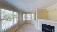 This three-floor home offers a thoughtfully designed layout with warm, neutral tones and practical finishes throughout. The living room is a standout space, featuring a graceful bay window arrangement that floods the room with natural light and offers views of the surrounding greenery. A tile-surround fireplace anchors the room, complemented by crown molding, textured ceilings, and soft wall-to-wall carpeting. The kitchen is well-appointed with rich oak cabinetry, granite-look countertops, stainless steel appliances including a range, over-the-range microwave, and refrigerator, as well as hardwood flooring that adds warmth to the space. Multiple carpeted bedrooms provide comfortable, versatile spaces, each featuring windows with blinds that allow for natural light and privacy. The primary bathroom includes a soaking tub set beneath a window, a wood-cabinet vanity, and hardwood flooring, while a second full bathroom offers a shower-tub combo with clean white finishes. The attached two-car garage provides generous storage and utility space with concrete floors and an automatic door opener. The home's consistent warm beige palette and classic design elements create a cohesive, welcoming atmosphere throughout all three levels.