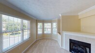 This three-floor home offers a thoughtfully designed layout with warm, neutral tones and practical finishes throughout. The living room is a standout space, featuring a graceful bay window arrangement that floods the room with natural light and offers views of the surrounding greenery. A tile-surround fireplace anchors the room, complemented by crown molding, textured ceilings, and soft wall-to-wall carpeting. The kitchen is well-appointed with rich oak cabinetry, granite-look countertops, stainless steel appliances including a range, over-the-range microwave, and refrigerator, as well as hardwood flooring that adds warmth to the space. Multiple carpeted bedrooms provide comfortable, versatile spaces, each featuring windows with blinds that allow for natural light and privacy. The primary bathroom includes a soaking tub set beneath a window, a wood-cabinet vanity, and hardwood flooring, while a second full bathroom offers a shower-tub combo with clean white finishes. The attached two-car garage provides generous storage and utility space with concrete floors and an automatic door opener. The home's consistent warm beige palette and classic design elements create a cohesive, welcoming atmosphere throughout all three levels.