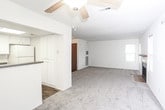 This single-floor unit offers a functional and well-organized layout designed for comfortable everyday living. The open-concept living and dining area is finished with wall-to-wall carpet and features a ceiling fan overhead, with natural light filtering in through a window that looks out to the surrounding neighborhood. The space flows seamlessly into the kitchen, which is separated by a partial wall and countertop bar. The galley-style kitchen is efficiently arranged with white cabinetry, granite-look countertops, a stainless steel sink, a white electric range, and a built-in microwave, all set atop durable wood-look flooring. Multiple bedrooms are found throughout the unit, each finished with plush carpeting and neutral wall tones. The bedrooms benefit from generous window placements, allowing ample natural light and neighborhood views. The unit includes two full bathrooms, both featuring white vanity cabinetry with dark countertops, a tub-shower combination, and wood-look flooring that complements the kitchen aesthetic. A fireplace is also visible in the living area, adding a warm focal point to the main gathering space. The overall palette of soft neutrals and clean finishes creates a bright, move-in-ready atmosphere throughout.