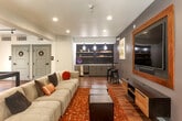 Located at 200 Winchester Cir in Los Gatos, CA, this single-floor community lounge is a well-appointed gathering space designed for both relaxation and entertainment. The open-plan layout accommodates a variety of social activities, anchored by a generously sized sectional sofa arranged atop a warm terracotta-toned area rug over light wood flooring that runs throughout the space.

A large flat-screen TV framed in natural wood is mounted on a slate-gray accent wall, complemented by a floating wood media console below. Across the room, a pool table serves as a central recreational feature, while a wall-mounted cue rack keeps equipment neatly organized nearby.

The wet bar area is a standout feature, showcasing a dramatic black hexagonal tile backsplash with open shelving, pendant lighting, and under-counter appliances — ideal for hosting events. A high-top table with bar stools offers an additional casual seating option.

Two sets of black-framed glass doors open directly to an outdoor patio, flooding the interior with natural light and providing views of the lush surrounding greenery. Recessed lighting throughout ensures a warm, inviting ambiance. Restroom facilities are conveniently accessible within the space, making this lounge a fully functional and thoughtfully designed communal retreat.