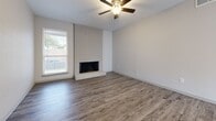 This single-story space is designed with a clean, neutral aesthetic and consistent wood-look flooring that flows throughout all rooms, creating a cohesive and easy-to-maintain interior. The main living area serves as a focal point, anchored by a floor-to-ceiling white painted brick fireplace that adds character and warmth to the otherwise minimalist space. A ceiling fan with integrated lighting is centrally positioned overhead, providing both air circulation and ambient light. Natural light filters in through windows fitted with blinds, adding brightness to the living areas.

The layout, visible in the 3D scan, reveals a practical floor plan connecting the living area to a kitchen, multiple additional rooms, and a bathroom. The kitchen area is positioned adjacent to the main living space. The additional rooms feature the same wood-look flooring, neutral wall tones, and windows that bring in natural light, making them versatile for various uses. One room includes a sliding glass door with vertical blinds, offering access to the exterior.

The bathroom is accessible via a hallway and includes a full tub-shower combination with white tile surround, toilet, and clean white walls. Throughout the space, white baseboards and neutral gray-beige walls contribute to a bright, move-in-ready atmosphere.