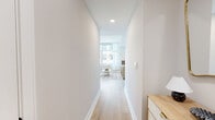 Located in the heart of Bethesda, MD, this well-appointed 2-bedroom, 2-bathroom residence offers a thoughtfully designed single-floor layout with a clean, contemporary aesthetic throughout. Light hardwood flooring flows seamlessly from the entry hallway into the main living areas, creating a bright and cohesive feel.

The open-concept kitchen and living room serves as the centerpiece of the home. The kitchen features two-tone cabinetry — white uppers paired with deep navy lowers — complemented by gold hardware, stainless steel appliances, a herringbone tile backsplash, and a window offering sweeping open-sky views. The living area receives abundant natural light through large windows framed by sheer white curtains, with views of the surrounding Bethesda cityscape.

The primary bedroom is a generously sized retreat with large floor-to-ceiling windows showcasing expansive outdoor views, and the second bedroom offers ample closet space and its own natural light. Both bedrooms feature light wood flooring and a calm, neutral palette.

The two bathrooms are distinctly styled: one showcases a glass-enclosed walk-in shower with marble-look tile and a dark vanity with gold accents, while the other features a full soaking tub with decorative tilework. Additional highlights include in-unit laundry, multiple closets, and two hallways for a practical, well-organized floor plan.
