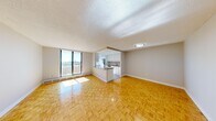 This 2-bedroom, 1-bathroom unit is thoughtfully laid out across a single floor, making efficient use of its compact footprint. Warm parquet flooring runs consistently throughout the living areas and bedrooms, lending a cohesive, classic look to the interior.

The open-concept living room and kitchen area forms the heart of the unit. A large floor-to-ceiling sliding glass door leads to a balcony, filling the space with natural light and offering expansive outdoor views. The kitchen is separated by a peninsula counter with a dark laminate surface, providing additional workspace and a casual dining option. Inside the kitchen, white cabinetry extends to the ceiling, offering ample storage, while stainless steel appliances — including a refrigerator, electric range, and built-in microwave — complement the clean, modern aesthetic. A window above the sink brings in additional natural light.

Both bedrooms are well-proportioned, each featuring parquet flooring, neutral walls, and windows with open views. Baseboard heating units run beneath the windows in both rooms.

The bathroom is clean and functional, featuring a full soaker tub with shower, a white vanity with drawers, a stone-toned countertop, and a well-lit mirror. The overall ambiance of the unit is bright, neutral, and move-in ready.