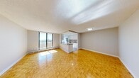 This 2-bedroom, 1-bathroom unit is thoughtfully laid out across a single floor, making efficient use of its compact footprint. Warm parquet flooring runs consistently throughout the living areas and bedrooms, lending a cohesive, classic look to the interior.

The open-concept living room and kitchen area forms the heart of the unit. A large floor-to-ceiling sliding glass door leads to a balcony, filling the space with natural light and offering expansive outdoor views. The kitchen is separated by a peninsula counter with a dark laminate surface, providing additional workspace and a casual dining option. Inside the kitchen, white cabinetry extends to the ceiling, offering ample storage, while stainless steel appliances — including a refrigerator, electric range, and built-in microwave — complement the clean, modern aesthetic. A window above the sink brings in additional natural light.

Both bedrooms are well-proportioned, each featuring parquet flooring, neutral walls, and windows with open views. Baseboard heating units run beneath the windows in both rooms.

The bathroom is clean and functional, featuring a full soaker tub with shower, a white vanity with drawers, a stone-toned countertop, and a well-lit mirror. The overall ambiance of the unit is bright, neutral, and move-in ready.