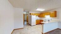 Located at 8091 Park Place Dr in Newburgh, Indiana, this single-story unit offers a practical and comfortable layout designed for everyday living. The kitchen is a central feature, equipped with warm-toned oak cabinetry spanning both upper and lower sections, white appliances including a Whirlpool refrigerator and electric range, and light-colored countertops. A peninsula counter separates the kitchen from the adjacent living area, providing a natural transition between the two spaces. The kitchen floor features neutral tile, and a ventilation hood is positioned above the range for added functionality.

The living area extends from the kitchen and is finished with neutral wall-to-wall carpeting, contributing to a cozy atmosphere. A ceiling fan with an integrated light fixture serves the space, and clean white walls provide a blank canvas throughout. The transition between tile and carpet at the kitchen boundary defines each area clearly.

The bathroom includes a walk-in shower stall with chrome fixtures, a toilet, and tile flooring, maintaining a clean, straightforward design. Textured ceilings are consistent throughout the unit, and wood-tone door trim adds warmth to the neutral color palette. The floor plan, visible in the 3D overview, reveals a well-organized arrangement of rooms connected by a central hallway.