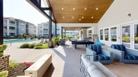 Located at 100 Vintage Alcoa Way in Alcoa, Tennessee, this outdoor amenity space offers a resort-style experience designed for relaxation and recreation. The centerpiece is a generously sized lap pool with vivid turquoise water, framed by a broad sun deck outfitted with lounge chairs and seating areas ideal for soaking up the Tennessee sun.

Adjacent to the pool is a large covered cabana structure, distinguished by its warm wood-paneled ceiling, exposed timber beams, and recessed lighting. This sheltered gathering area is furnished with comfortable upholstered seating, a pool table, and a mounted flat-screen television, creating a versatile space for both leisure and socializing. The cabana opens directly onto the pool deck, blurring the boundary between indoor comfort and outdoor living.

Surrounding the pool and cabana, thoughtfully curated landscaping features blooming hydrangeas, ornamental shrubs, and manicured plantings that add color and texture to the environment. A pergola structure accented with string lights provides an additional shaded retreat. Black wrought-iron fencing encloses the space, lending a sense of privacy and security.

The multi-story residential buildings visible in the background, clad in gray lap siding and brick accents with private balconies, provide an attractive architectural backdrop. The overall ambiance is bright, open, and welcoming, reflecting a well-appointed community amenity space.