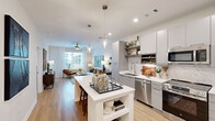 Located at 1515 Rollick Rd in Cary, NC, this well-appointed one-bedroom, one-bathroom residence offers a thoughtfully designed single-floor layout. Light wood flooring runs throughout, creating a warm and cohesive aesthetic across all rooms.

The open-concept kitchen and living area form the heart of the home. The kitchen is outfitted with flat-front grey cabinetry that extends to the ceiling, a marble-style tile backsplash, stainless steel appliances including a French door refrigerator, a built-in microwave, and a range, complemented by open shelving for display and storage. A central island with a white quartz countertop, bar seating, and integrated storage serves as both a functional workspace and a casual dining spot. Stylish glass pendant lights hang above, adding a contemporary touch.

The living room is bathed in natural light from large windows with outdoor views, and features a ceiling fan overhead. The bedroom is a comfortable retreat, also benefiting from generous windows, a ceiling fan, and ample closet space.

The bathroom is sleek and elongated, featuring a white vanity with grey cabinetry, a marble-tiled walk-in shower with frameless glass doors, and light wood flooring that carries through from the rest of the home.