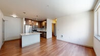 Located at 4745 40th Ave SW in Seattle's West Seattle neighborhood, this one-bedroom, one-bathroom apartment offers a well-designed single-floor layout with a thoughtful mix of materials and finishes throughout. The open-concept kitchen serves as the heart of the unit, showcasing rich dark wood cabinetry, a granite-topped island with pendant lighting, stainless steel appliances including a refrigerator, range, microwave, and dishwasher, and a mosaic tile backsplash. Track lighting illuminates the kitchen, while warm hardwood flooring extends through the main living areas. The bedroom is a calm, neutral space with plush carpeting, a wide window that brings in natural light and exterior views, and a baseboard heater for year-round comfort. A dedicated closet with built-in shelving provides practical storage directly off the bedroom. The bathroom is finished with dark wood vanity cabinetry, a granite countertop, a large mirror, hardwood flooring, and a full tub-shower combination with clean white tile surround. The overall ambiance is modern and functional, with a consistent palette of warm wood tones, neutral walls, and quality finishes that create a cohesive and comfortable living environment.