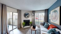 This thoughtfully designed 1-bedroom, 1-bathroom single-story residence offers a comfortable and stylish living environment across a compact yet efficiently utilized floor plan. The living room serves as the heart of the home, featuring a corner fireplace with a white brick surround, wood-style flooring, and multiple large windows that flood the space with natural light. A bold teal accent wall adds a striking visual element, complemented by a textured ceiling and sliding glass door leading to a private balcony. The kitchen is outfitted with rich dark cabinetry, granite-style countertops, a subway tile backsplash, and stainless steel appliances. A dedicated closet adjacent to the kitchen conveniently houses in-unit laundry. The bedroom offers plush carpeting, a ceiling fan, and a sliding glass door opening to its own balcony access, providing an additional outdoor retreat. The bathroom features a dark wood vanity with a light stone countertop, a large framed mirror, and modern light fixtures. A dedicated closet rounds out the layout. Throughout the space, wood-style flooring, neutral tones, and consistent design choices create a cohesive and modern ambiance.