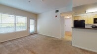 This single-floor residence offers a thoughtfully organized layout that balances functionality and comfort. The galley-style kitchen is efficiently designed with light natural wood cabinetry, dark granite-style countertops, and black appliances including a gas range, built-in microwave, and dishwasher, all set atop light tile flooring that runs throughout the kitchen and bathrooms.

The living area is generously sized, featuring warm beige carpeting and neutral-toned walls that create a bright, welcoming atmosphere. A pendant light fixture adds a touch of character, while a door provides direct access to an outdoor area, bringing in natural light and a sense of openness. Additional carpeted rooms serve as comfortable bedrooms, each with ample wall space, windows that invite natural light, and easy access to the hallways.

The residence includes two full bathrooms finished in a clean, neutral palette. Both feature light wood vanities with white countertops and tile flooring. One bathroom includes a shower and grab bar, while the other offers a full tub-shower combination with classic white tile surround and chrome fixtures, adding practicality for everyday use.

Overall, the space presents a clean, move-in-ready interior with consistent finishes, soft neutral tones, and a functional floor plan well-suited for comfortable residential living.