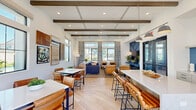 Located at 400 Stanford Crossing in Lathrop, CA, this single-floor space combines a kitchen, dining room, and living room in a cohesive, open-plan layout designed for both comfort and style. Exposed wood beams run across the white ceilings throughout, lending a warm architectural character to the interior while reinforcing a sense of vertical openness.

The kitchen is a standout feature, anchored by a large island with a quartz countertop and leather bar seating. Crisp white shaker cabinetry lines the walls, complemented by a vivid cobalt blue subway tile backsplash. Industrial-style pendant lights hang above the island, and a stainless steel refrigerator completes the functional layout. Large glass sliding doors open directly to an outdoor patio, flooding the space with natural light and creating a seamless indoor-outdoor connection.

The dining area sits adjacent to the kitchen and benefits from tall windows that frame outdoor greenery, filling the room with abundant daylight. A curated gallery wall adds an artistic focal point alongside the natural light.

The living room is thoughtfully designed with a bold blue geometric accent wall housing a wall-mounted television, flanked by contemporary sconce lighting. Large windows with plaid drapery bring in further natural light and neighborhood views. Light wood-toned flooring flows throughout, unifying the entire space with a clean, modern aesthetic.