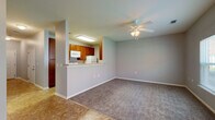 This two-floor residence offers a practical and comfortable layout designed for everyday living. The main level opens into a combined living and dining area finished with plush carpeting and tile flooring, illuminated by a ceiling fan with integrated lighting. The kitchen is accessible via a pass-through counter that overlooks the living space, providing an open and connected feel. Inside, the galley-style kitchen is well-appointed with warm wood cabinetry, light countertops, a full suite of white appliances including an electric range, microwave, refrigerator, and dishwasher, and a stainless steel sink. A glass door on the main level provides direct access to the exterior. A staircase with a white-painted banister and handrail connects the two floors via a hallway with tile flooring. The upper level hosts carpeted bedrooms, each equipped with ceiling fans. At least one bedroom features dual closets, including a walk-in closet with shelving. Two full bathrooms are present, each offering a single-sink vanity with wood cabinetry, a toilet, and a tub-shower combination with tile surround. A dedicated laundry room accommodates a full-size washer and dryer with overhead wire shelving. Neutral gray walls and white trim are consistent throughout, giving the space a clean, cohesive appearance.