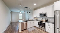 Located at 1400 N Main St in Keller, TX, this thoughtfully designed one-bedroom, one-bathroom residence offers a clean, modern aesthetic throughout. The open-concept kitchen and living area serves as the heart of the home, anchored by a sleek kitchen featuring white shaker cabinetry, dark granite countertops, a subway tile backsplash, and a full suite of stainless steel appliances including a French door refrigerator, electric range, built-in microwave, and dishwasher. A peninsula with pendant lighting adds both style and functionality, while wood-look flooring and recessed lighting create a bright, cohesive atmosphere. The living area offers ample space and natural light from a large window. The bedroom is a comfortable retreat with a ceiling fan, a generous window with outdoor views, and direct access to both the bathroom and a spacious walk-in closet outfitted with wrap-around shelving and carpeted flooring. The bathroom features white cabinetry, dark granite countertops, and a large vanity mirror. A dedicated laundry room with shelving completes the layout, offering added convenience. The hallway and entrance tie the space together with a clean, well-organized flow.