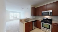 Located at 460 River in Andover, Massachusetts, this single-floor residence offers a thoughtfully designed open-concept layout that seamlessly connects the kitchen and living area. The kitchen is a standout feature, equipped with rich dark wood cabinetry, granite countertops with a tile backsplash, and a full suite of stainless steel appliances including a gas range, built-in microwave, dishwasher, and refrigerator. A peninsula with an undermount sink serves as a natural divider between the kitchen and the carpeted living space, which benefits from large windows that invite generous natural light. Track lighting overhead adds a modern touch to the open living area. The bedrooms are comfortably sized, each featuring plush wall-to-wall carpeting and windows fitted with blinds for privacy and light control. The bathroom is finished with clean, contemporary details, including a rich wood vanity, white countertops, a large mirror, and tile flooring. The overall palette throughout the residence is neutral and bright, with white walls and light-toned finishes creating an airy, welcoming ambiance. The layout, as seen in the dollhouse view, is efficiently organized with well-defined living, sleeping, and utility zones.