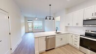 This well-appointed single-floor residence offers a thoughtfully designed layout spanning a comfortable footprint, accommodating two bedrooms, two bathrooms, and three closets. The open-concept kitchen and living area serves as the heart of the unit, where crisp white shaker cabinetry, light quartz countertops, and a peninsula island create a clean, modern aesthetic. A suite of stainless steel appliances—including a French door refrigerator, electric range, over-the-range microwave, and dishwasher—completes the kitchen. A stylish multi-pendant black light fixture anchors the island, adding a contemporary accent. Light wood-tone flooring flows consistently throughout the space, enhancing its bright, cohesive feel.

The living area benefits from natural light through large windows and direct access to a private balcony. Both bedrooms are generously proportioned, featuring ceiling fans, windows with outdoor views of surrounding greenery, and neutral white walls. The spacious primary bedroom includes its own dedicated closet. The two bathrooms maintain the unit's clean design language, with white cabinetry, stone-surface vanities, and black hardware accents. Hallways connect the rooms efficiently, and the three closets provide ample built-in storage throughout.