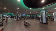 Located at 10625 Calle Mar De Mariposa, this professional fitness facility offers a comprehensive single-floor workout environment designed to accommodate a wide range of training needs. The main floor is expansive and open, featuring a striking dark ceiling with a bold circular design element accented by ambient teal and green lighting that gives the space a sleek, modern atmosphere. Recessed lighting throughout ensures the entire floor is well-illuminated.

The cardio zone is well-stocked with rows of treadmills and elliptical machines, each equipped with individual display screens for an engaging workout experience. The strength training area includes a wide variety of resistance machines, cable stations, and benches, catering to both beginner and advanced athletes. A dedicated free weights section features a colorful and organized array of kettlebells, BOSU balls, step platforms, and resistance tools, displayed along a mirrored wall for easy access.

Full-length mirrors line multiple walls, enhancing the sense of space and allowing users to monitor their form. A separate glass-enclosed studio with hardwood flooring provides a dedicated space for group classes or personal training sessions. Multiple mounted flat-screen televisions are positioned throughout the facility, contributing to an engaging and energetic environment. The durable rubber flooring throughout the main workout area ensures both safety and comfort during exercise.