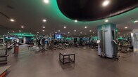 Located at 10625 Calle Mar De Mariposa, this professional fitness facility offers a comprehensive single-floor workout environment designed to accommodate a wide range of training needs. The main floor is expansive and open, featuring a striking dark ceiling with a bold circular design element accented by ambient teal and green lighting that gives the space a sleek, modern atmosphere. Recessed lighting throughout ensures the entire floor is well-illuminated.

The cardio zone is well-stocked with rows of treadmills and elliptical machines, each equipped with individual display screens for an engaging workout experience. The strength training area includes a wide variety of resistance machines, cable stations, and benches, catering to both beginner and advanced athletes. A dedicated free weights section features a colorful and organized array of kettlebells, BOSU balls, step platforms, and resistance tools, displayed along a mirrored wall for easy access.

Full-length mirrors line multiple walls, enhancing the sense of space and allowing users to monitor their form. A separate glass-enclosed studio with hardwood flooring provides a dedicated space for group classes or personal training sessions. Multiple mounted flat-screen televisions are positioned throughout the facility, contributing to an engaging and energetic environment. The durable rubber flooring throughout the main workout area ensures both safety and comfort during exercise.