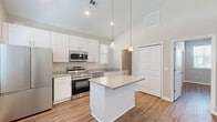 Located at 133 Watercolor Blvd in Hardeeville, SC, this well-designed single-story home offers a thoughtful layout that maximizes every inch of its comfortable footprint. Soaring vaulted ceilings in the open-concept kitchen and living area create an impressive sense of spaciousness and allow natural light to fill the space. The kitchen is a standout feature, showcasing crisp white shaker cabinets, granite countertops, a central island with pendant lighting, and a full suite of stainless steel appliances including a refrigerator, range, and microwave. Warm hardwood-style flooring runs continuously throughout the home, adding cohesion and a clean aesthetic. The living area benefits from dual windows framing views of the surrounding greenery, enhancing the airy, welcoming atmosphere. The generously sized bedroom features multiple windows that flood the room with natural light and offer outdoor views, complemented by the same neutral tones and hardwood-style flooring. The bathroom is finished with a white vanity topped with granite, a glass-enclosed walk-in shower, and consistent design details. A dedicated laundry area with a stacked washer and dryer unit adds practical convenience. The home presents a modern, move-in ready aesthetic throughout.