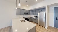 Located at 4000 Emerson Dr in Mount Wolf, PA, this well-appointed single-floor residence offers one bedroom and two bathrooms within a thoughtfully designed layout. The open-concept kitchen serves as a central highlight, featuring gray shaker-style cabinetry, crisp white quartz countertops, a peninsula with an undermount sink, globe pendant lighting, and a full suite of stainless steel appliances including a range, microwave, dishwasher, and refrigerator. Light-toned luxury vinyl plank flooring flows throughout the main living areas, adding warmth and continuity. The living room is bright and open, with a sliding glass door fitted with vertical blinds that allows natural light to fill the space. The bedroom is carpeted for comfort, includes a ceiling fan, a wide window with horizontal blinds, and a closet with built-in shelving. Both bathrooms are designed with accessibility in mind, featuring grab bars, a tub with a bench seat and handheld shower, LVP flooring, and clean white finishes. The neutral color palette and modern fixtures throughout create a clean, contemporary ambiance well-suited for comfortable everyday living.