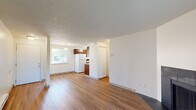 This well-appointed 1-bedroom, 1-bathroom unit is thoughtfully designed to maximize every inch of its single-floor layout. The open-concept living and kitchen area serves as the heart of the home, with warm hardwood-style flooring flowing seamlessly throughout. The living room is highlighted by a striking black tile-surround fireplace, which adds both character and warmth to the space. A sliding glass door floods the room with natural light and provides outdoor access, further enhancing the bright and airy atmosphere. The kitchen features rich, dark wood cabinetry, a full-size refrigerator, and a range, with ample counter and storage space efficiently arranged in a galley-style layout. A pendant light and ceiling fixture provide functional illumination. The bedroom offers a practical closet with built-in shelving and benefits from natural light through a window. The full bathroom is equipped with a vanity featuring granite-style countertops, a toilet, and a shower-tub combination. A dedicated utility room houses the water heater, providing added convenience. Textured ceilings are present throughout, and the overall color palette of white walls and warm flooring creates a clean, neutral ambiance.