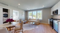 This well-appointed single-floor residence offers a thoughtfully designed open-concept layout that seamlessly connects the living, dining, and kitchen areas. The living space is anchored by a large multi-pane window that floods the room with natural light and frames views of surrounding greenery, creating a warm and airy atmosphere throughout. Light hardwood flooring runs continuously across the entire unit, enhancing the sense of cohesion and space.

The kitchen is sleek and modern, featuring white flat-front cabinetry, a white subway tile backsplash, and a full suite of stainless steel appliances including a range, over-the-range microwave, dishwasher, and refrigerator. Adjacent to the kitchen, the living area provides ample room for both relaxation and dining.

The bedroom is a serene retreat, bathed in natural light through large windows offering outdoor views, and finished with the same warm hardwood flooring. The bathroom features a full soaking tub with a classic white subway tile surround accented by contrasting taupe tile bands, delivering a clean and polished aesthetic.

A dedicated in-unit laundry closet with a stacked washer and dryer adds everyday convenience. Neutral gray walls throughout the space create a calm, contemporary backdrop that complements the overall modern design sensibility.