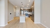 This single-floor space presents a cohesive, contemporary design highlighted by light wood-style flooring that flows seamlessly throughout. The kitchen serves as a central feature, equipped with stainless steel appliances including a refrigerator, range, and microwave. Taupe-toned shaker cabinetry lines the walls, complemented by a white subway tile backsplash and a granite-topped island with pendant lighting overhead, offering both additional prep space and a casual seating area. Recessed lighting keeps the kitchen bright and functional.

The bedroom is a calm, neutral space with warm beige walls and a ceiling fan. A double window frames views of a pool area with palm trees, allowing ample natural light to fill the room.

The bathroom is finished with a tiled tub-shower surround in a soft linear pattern, wood-look tile flooring, a granite-topped vanity with gray cabinetry, and a mirror above. The fixtures and grab bar reflect a clean, practical design.

The 3D floor plan reveals a well-organized layout with an efficient flow between the kitchen, living areas, and private rooms, making the most of the available single-level space.