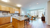 This single-floor residence is designed with an open-concept layout that seamlessly connects the kitchen, dining, and living areas into one cohesive space. The kitchen is equipped with warm maple cabinetry, white appliances, a double sink, and a granite-topped island with bar seating, providing both prep space and casual dining functionality. Adjacent to the kitchen, the dining area accommodates a round table with mixed seating, while the living room features large windows that invite substantial natural light and offer views of the surrounding neighborhood. Hardwood-style flooring extends throughout the main living areas, contributing to a bright and unified aesthetic.

The unit includes two bedrooms, each carpeted for comfort. The primary bedroom benefits from a wide window overlooking the exterior, while the secondary bedroom offers a quieter, more compact layout. Both rooms provide ample space for standard furnishings. The full bathroom features hardwood-style flooring, a vanity with warm wood cabinetry, and a tub-shower combination. A dedicated laundry area includes wire shelving for storage and accommodates a full-sized washer, adding practical convenience to the overall floor plan.