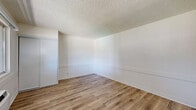 Located at 43321 Sierra Hwy in Lancaster, California, this studio unit offers a practical and efficiently designed single-floor layout comprising a living area and a full bathroom. The main living space features light-toned, wood-style plank flooring that runs throughout, lending warmth and continuity to the interior. Crisp white walls and a textured popcorn ceiling frame the room, while a large sliding window allows ample natural light to filter in and provides views of the outdoor surroundings, including a glimpse of a balcony railing and mature trees. A wall-mounted HVAC unit ensures climate control, and a baseboard heater adds supplemental warmth. A built-in closet with sliding doors provides dedicated storage space. Adjacent to the main living area, a compact kitchenette is equipped with white cabinetry and a stainless steel range, offering essential cooking functionality. The bathroom is cleanly finished with white square tile walls surrounding a full soaking tub and shower combination, complemented by a single-sink vanity with under-cabinet storage, a large mirror, and matching wood-style flooring. The electrical panel is conveniently accessible within the living area. Overall, the unit presents a clean, updated aesthetic well-suited for efficient, comfortable living.
