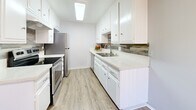 Located at 23930 Ocean Ave in Torrance, CA, this single-floor unit offers a clean, modern aesthetic throughout its well-maintained interior. The living area is bright and open, featuring warm laminate wood flooring and a large sliding glass door dressed with vertical blinds that allows abundant natural light to fill the space. A ceiling fan with integrated lighting adds both function and comfort to the living area.

The kitchen is a standout feature, designed in a galley layout with crisp white shaker cabinetry, light stone-finish countertops, a tile backsplash with subtle patterning, and stainless steel appliances including a refrigerator and range. A skylight panel above keeps the kitchen bright and inviting.

The bedrooms continue the laminate flooring theme and are dressed in a neutral gray palette with white trim. One bedroom includes a mirrored sliding closet, while multiple rooms feature large windows with vertical blinds providing ample light and privacy. The bathroom is accessible from the hallway and offers white cabinetry, a single vanity with a mirror, and updated lighting fixtures.

Throughout the unit, textured ceilings, consistent flooring, and a cohesive cool-gray color scheme create a tidy, move-in-ready environment suited for comfortable everyday living.