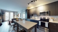 This thoughtfully designed single-floor residence offers a seamless blend of modern aesthetics and functional living. The open-concept kitchen is a standout feature, outfitted with dark flat-panel cabinetry extending to the ceiling, stainless steel appliances including a range, microwave, and refrigerator, a white subway tile backsplash, and a large kitchen island with quartz countertops that doubles as a dining and prep area. Track lighting overhead adds a contemporary touch while illuminating the space effectively.

The living room offers a welcoming atmosphere with light wood-style flooring, large windows and a glass door that invite natural light and provide outdoor access. Bold abstract artwork and eclectic furnishings contribute to the room's vibrant character.

Two bedrooms provide comfortable retreats, each featuring light-toned walls, natural light from large windows, and light wood flooring. One bedroom includes a built-in desk area, while the other offers ample wall space and convenient storage.

The primary bathroom is elegantly finished with marble-style tile flooring, a double-sink vanity with dark cabinetry, and a walk-in glass-enclosed shower with white subway tile. The secondary bathroom features the same marble-style flooring alongside a full tub-shower combination and a single vanity, completing this well-appointed residence.