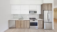 Located at 800 S Harvard Blvd in the Koreatown neighborhood of Los Angeles, this modern single-floor unit offers a clean, contemporary design throughout. Light wood flooring runs continuously across the living spaces, complementing the crisp white walls and creating a bright, airy atmosphere. The open-concept living and dining area is generously proportioned, bathed in natural light from large windows and glass sliding doors that open to a private balcony with views of surrounding greenery. The kitchen is thoughtfully designed with a seamless blend of white upper cabinetry and warm wood-toned lower cabinets, accented by a hexagonal tile backsplash and durable quartz countertops. Stainless steel appliances, including a range, microwave, dishwasher, and refrigerator, complete the functional cooking space. The bedrooms are well-sized and bright, each featuring windows that bring in ample natural light. One bedroom includes a walk-in closet with built-in shelving. The bathrooms are finished with large-format dark tile flooring, vertically stacked white subway tile in the tub surrounds, wood-toned vanities, and backlit LED mirrors, adding a refined, contemporary touch to the overall aesthetic.