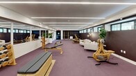 Located at 1188 King St in Greenwich, Connecticut, this upscale fitness facility offers a thoughtfully designed, open-plan space that seamlessly blends function with refined aesthetics. The interior is defined by a striking linear LED lighting system recessed into a clean white ceiling, casting even, modern illumination throughout the room. Plush mauve-toned carpet covers the floor, lending warmth and comfort underfoot across the generously proportioned workout area. A standout design feature is the lush living green wall, which spans a full section of the space and adds a vibrant, biophilic element alongside a wall-mounted display screen. Floor-to-ceiling mirrors along one wall visually expand the room and enhance the workout experience. The facility is equipped with premium wooden-framed fitness equipment, including treadmills, rowing machines, stationary bikes, adjustable benches, and a well-stocked dumbbell rack. A dedicated lounge area furnished with sleek white armchairs provides a space for rest and recovery. A row of clerestory windows along one wall allows natural light to filter in, connecting the interior to the outdoors. The overall ambiance is one of boutique luxury, combining professional-grade fitness amenities with sophisticated interior design elements.