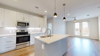 Located in Irving, TX, this well-appointed 2-bedroom, 2-bathroom residence offers a thoughtfully designed single-floor layout with modern finishes throughout. The open-concept kitchen is a standout feature, showcasing a large center island with a quartz countertop and undermount sink, crisp white shaker cabinetry extending to the ceiling, a classic subway tile backsplash, and a full suite of stainless steel appliances including a french door refrigerator, electric range, built-in microwave, and dishwasher. Stylish pendant lights hang above the island, adding warmth to the bright, airy space. Light-toned hardwood-style flooring flows through the main living areas, while the living room offers access to a private balcony through glass-paneled doors, filling the space with natural light. Both bedrooms are carpeted and include ceiling fans and windows with outdoor views. The primary bedroom features its own closet with built-in shelving and hanging rods. The bathrooms are elegantly finished, with one featuring a soaking tub surrounded by large-format marble-look tile. Two dedicated closets and a hallway round out this efficient, contemporary home.