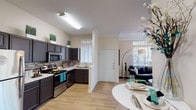 This single-story residence in the 77339 zip code of Kingwood, Texas, offers a thoughtfully designed open-concept floor plan with a seamless flow between the kitchen, dining, and living areas. The kitchen is outfitted with dark espresso cabinetry, a mosaic tile backsplash, stainless steel appliances including a refrigerator, gas range, and built-in microwave, along with light wood-look flooring that extends throughout the main living spaces. A dedicated laundry area with a stacked washer and dryer is conveniently accessible just off the kitchen. The living room is a standout feature, bathed in natural light through expansive windows with transom panes that frame picturesque views of surrounding trees. Crown molding and a ceiling fan add a polished finish to the space. The bedrooms offer a quieter retreat, carpeted for comfort, with windows that invite natural light and views of the wooded surroundings. The bathroom includes a soaking tub and shower combination, dark vanity cabinetry, built-in shelving, and wood-look flooring. Throughout the home, neutral tones, high ceilings, and abundant natural light create a bright and welcoming ambiance that connects the interior to the lush, tree-lined outdoor environment.