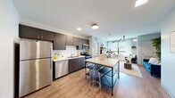 Located at 505 E St Louis St in Springfield, MO, this thoughtfully designed 3-bedroom, 3-bathroom unit offers a well-organized single-floor layout. The open-concept kitchen and living area serves as the heart of the space, featuring dark espresso cabinetry, stainless steel appliances including a refrigerator, dishwasher, range, and microwave, paired with light-toned countertops and light wood-look flooring that flows throughout the common areas. A freestanding island with a marble-style top provides additional prep and dining space. The living area is bathed in natural light from large windows dressed with sheer curtains, creating a bright and welcoming atmosphere. Each of the three bedrooms offers carpeted flooring and a private bathroom, with each bathroom featuring a dark-cabineted vanity, mirror, and a clean white walk-in tile shower. One bedroom includes a built-in desk setup, ideal for studying or working from home. The unit also includes a dedicated laundry area and utility room. A hallway connects the private spaces efficiently. The overall aesthetic is clean and contemporary, with a neutral palette that balances modern finishes and functional design throughout.