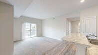 Located at 1900 Breccan Meadows Drive in Columbus, OH, this one-bedroom, one-bathroom residence offers a thoughtfully designed single-floor layout. The open-concept kitchen serves as the heart of the home, featuring dark espresso cabinetry, granite-style countertops, a peninsula with bar seating, and black stainless appliances including a range, microwave, and refrigerator. Warm hardwood-style flooring flows through the kitchen and into the main living areas, creating a cohesive and inviting atmosphere. The spacious living area is finished with plush carpeting and features a sliding glass door that opens to a private balcony, allowing natural light to fill the room and offering views of the surrounding community. The bedroom is carpeted and comfortably sized, with a large sliding closet door providing generous storage space and a window that brings in additional natural light. The bathroom is clean and functional, equipped with a full tub-shower combination featuring built-in shelving and chrome fixtures, complemented by tile-style flooring. A connecting hallway ties the layout together efficiently. This residence offers a practical and comfortable living environment with modern finishes throughout.