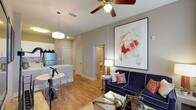 This 2-bedroom, 2-bathroom single-floor residence offers a well-designed open-concept layout that seamlessly integrates the living, dining, and kitchen areas into one cohesive and functional space. The living area is anchored by warm hardwood-style flooring and neutral toned walls that create a bright, welcoming ambiance. A ceiling fan with integrated lighting adds both practicality and a classic touch to the main living space, which also features a large statement artwork that serves as a bold focal point. The kitchen is outfitted with stainless steel appliances, ample cabinetry, and a peninsula-style counter with seating, making it ideal for casual dining and entertaining. Pendant lighting over the counter adds a modern accent to the space. A dedicated dining area sits adjacent to the kitchen, completing the open living zone. A hallway leads to the two private bedrooms and bathrooms, offering a clear separation between living and sleeping areas. The overall design balances contemporary style with everyday comfort, making this residence a practical and visually appealing home.