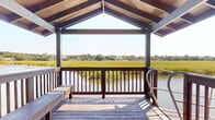 Located at 997 Johnnie Dodds Blvd in Mount Pleasant, South Carolina, this waterfront dock and pavilion structure offers an immersive Lowcountry experience defined by stunning tidal marsh views and direct water access. The single-level outdoor space centers around a covered pavilion featuring a distinctive gabled roof with exposed wooden beam framing, providing both shade and an open, airy feel. Built-in wooden bench seating lines the perimeter of the pavilion, making it an ideal spot for relaxing and taking in the expansive landscape.

The structure connects to a floating dock via a gently sloped gangway equipped with stainless steel handrails, allowing for easy water access regardless of tidal conditions. A separate open deck extends from the main structure, offering unobstructed panoramic views of the surrounding salt marsh and tidal creek. The golden green marsh grasses stretch broadly across the horizon, framing a tranquil waterway that winds through the landscape.

A long wooden boardwalk with dark-stained railings leads from the property through a canopy of mature, moss-draped trees to the waterfront, enhancing the sense of arrival and connection to the natural environment. Together, these elements create an exceptional outdoor retreat that embodies the natural beauty and relaxed charm of the South Carolina Lowcountry.