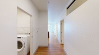 This well-designed two-bedroom, one-bathroom unit offers a thoughtfully organized single-floor layout with a clean, contemporary aesthetic. Warm hardwood-style flooring runs consistently throughout, lending cohesion and a sense of continuity across all rooms.

The kitchen features dark espresso cabinetry, black appliances including a refrigerator and electric range, and a spacious countertop with a double-basin stainless steel sink that opens toward the living area, creating an efficient and connected kitchen-living space. Recessed lighting illuminates the kitchen, adding a polished touch.

The living area benefits from abundant natural light and direct access to a private balcony through full-height sliding glass doors, offering open views of the surrounding neighborhood and tree canopy. The balcony features a cable-style railing, providing an unobstructed outdoor perspective.

Both bedrooms are bright and cleanly finished with white walls. The primary bedroom includes a dedicated closet with a wire shelving system. A dedicated laundry room houses a full-size front-loading washer and dryer with additional wire shelving above.

The bathroom includes a full tub-shower combination, a wood-toned vanity with a white countertop, and hardwood-style flooring consistent with the rest of the unit.