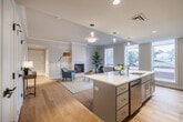 Located at 119 W Court St in Ithaca, NY, this thoughtfully designed 2-bedroom, 2-bathroom residence offers a clean, modern aesthetic throughout its well-utilized single-floor layout. The open-concept kitchen and living area serves as the heart of the home, featuring light gray shaker cabinetry, a white quartz waterfall island with bar seating, stainless steel appliances, and warm hardwood flooring. Pendant lighting and large windows flood the kitchen with natural light. The adjacent living room is anchored by a sleek built-in fireplace and crown molding, with expansive windows offering views of the surrounding Ithaca neighborhood. The primary bedroom is a comfortable, carpeted retreat with a large window framing outdoor views. The second bedroom, also carpeted, is a bright, serene space with ample natural light. Both bathrooms are finished in light tile with white cabinetry and modern fixtures; one features an accessible roll-in shower with grab bars and an illuminated vanity mirror. A hallway connects all spaces efficiently. The residence combines contemporary finishes with practical design, making it a well-appointed home in the heart of Ithaca.
