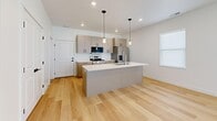 Located at 401 W Center St in Hyde Park, Utah, this contemporary two-story home offers three bedrooms and three bathrooms with a clean, modern aesthetic throughout. The main floor houses the combined kitchen and living area, where light hardwood flooring, recessed lighting, and crisp white walls set a bright, welcoming tone. The kitchen is outfitted with stainless steel appliances including a gas range, microwave, and refrigerator, complemented by quartz countertops and taupe cabinetry with sleek matte black hardware. The upper floor contains the bedrooms and laundry room. The generously sized primary bedroom features light hardwood floors and a walk-in closet with built-in shelving and a window that brings in natural light. Additional bedrooms are carpeted and include double-door closets and horizontal windows. The three bathrooms are finished in a modern style, with backlit vanity mirrors, quartz countertops, taupe cabinetry, and marble-style tiled tub surrounds. Black hardware accents throughout provide a cohesive design touch. A dedicated laundry room on the upper floor adds convenience. The home's consistent use of light tones, quality finishes, and functional layout creates a polished and comfortable living environment.